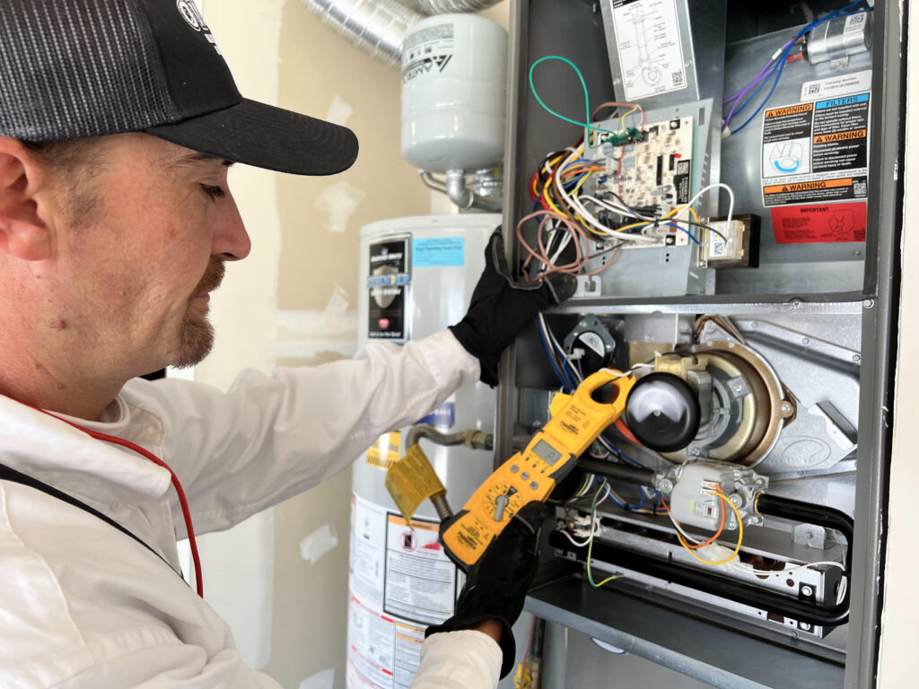 HVAC technician using a yellow multimeter to test electrical components inside an air handler unit.
