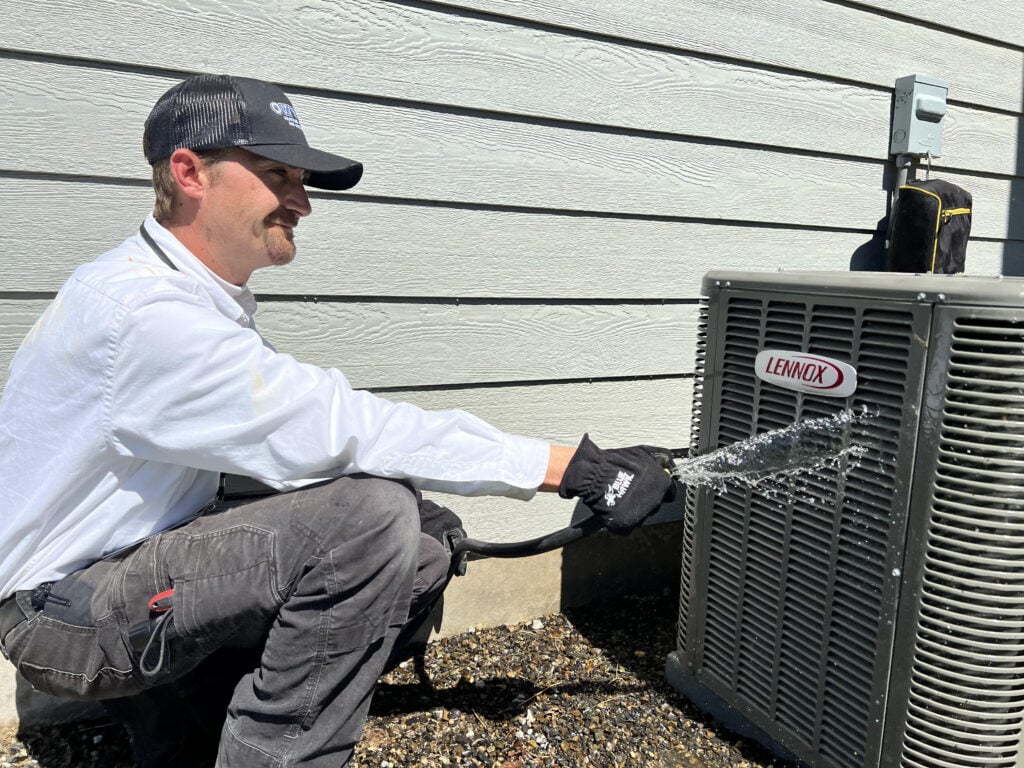 HVAC technician in white shirt and black cap inspecting a Lennox air conditioning unit outside residential home.
