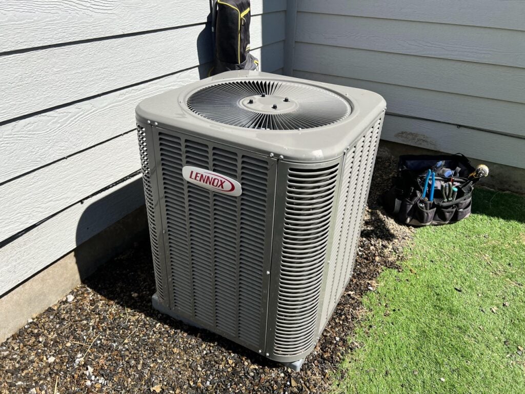 2023 Energy Tax Credit 2 Lennox central air conditioning condenser unit installed against white vinyl siding with service equipment nearby.