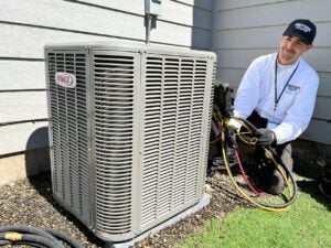 HVAC technician in white shirt and cap performs maintenance on outdoor Lennox air conditioning unit with diagnostic equipment and hoses.